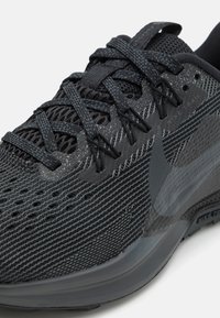 Zwarte hardloopschoen met een textuur van mesh bovenkant, versterkte naden en een opvallend Nike-logo. Beschikt over een gevoerde zool en duurzame veters.