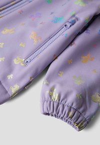 Nærbilde av ermet på en lilla jakke med elastisk mansjett, en glidelåslomme og skinnende flerfargede mønstre av enhjørninger og sløyfer.