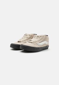 Beige høyhælte joggesko med snører, med en svart gummisåle og hvit side stripe detalj. Laget av semsket skinn og kanvasmaterialer.