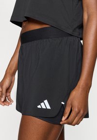 Μαύρο σορτς τρεξίματος με ελαστική μέση, με λευκό λογότυπο τριών ρίγες στο τελείωμα. Ελαφρύ ύφασμα με ομαλή υφή.