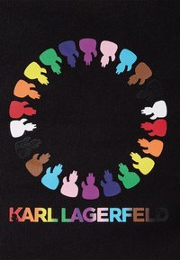 Černé plátno má kruhový vzor barevných siluet rukou v různých odstínech pleti, s nápisem "KARL LAGERFELD" v iridiscentním písmu pod ním.