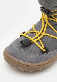 Chaussure d'extérieur grise avec une tige en tissu texturé, dotée de lacets élastiques jaunes et d'une semelle en caoutchouc avec un motif légèrement rugueux.