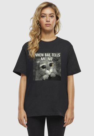 T-shirt in cotone nero con una grande illustrazione di un gatto con occhi grandi e didascalia, maniche corte e vestibilità comoda.