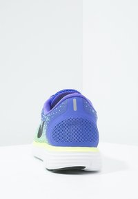 Chaussure de sport violette avec tige en mesh, logo swoosh noir, semelle blanche et accents jaunes. Elle dispose d'un col rembourré et d'un talon texturé.