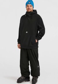 Fekete dzseki kapucnival, rugalmas mandzsettákkal és zsebből; fekete nadrággal párosítva. Kék kötött sapka háromszögletű logóval. Fekete csizma.