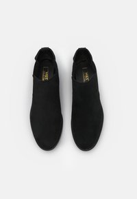 Pár černých suede slip-on kotníkových bot s kulatou špičkou a poutky, označených M&S Collection, zobrazených shora na bílém pozadí.
