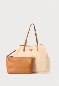 Beige faux fur tote taske med brune læderdetaljer, som har to lange håndtag og en lille brune læderlynlåspung, der er mærket "GUESS."