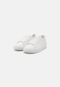 White sneakers featuring a textured upper with a circular pattern, classic lacing system, and a thick, white rubber sole.