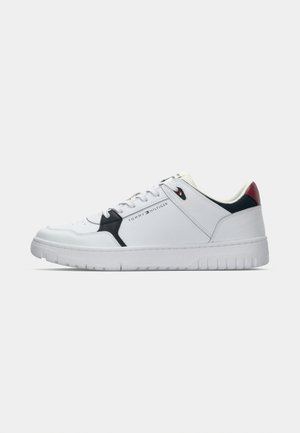 Zapatilla baja blanca con acentos en negro y rojo, marcada con "Tommy Hilfiger" en el lateral, y una suela blanca gruesa.