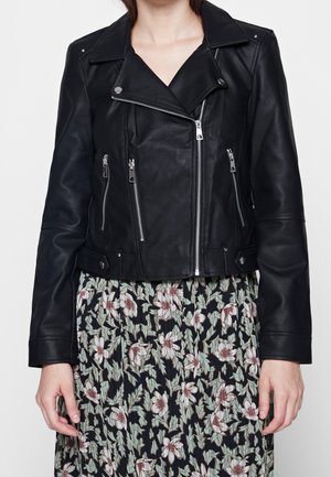 Sort læderjakke med asymmetrisk frontlynlås og sølvhardware båret over en sort kjole med blomsterprint.
