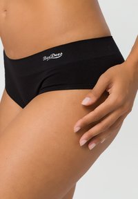 Schwarze Baumwollunterwäsche mit einem breiten elastischen Bund, der das "BeeDees"-Logo trägt. Glatte Textur, Hipster-Schnitt und körpernahe Passform.