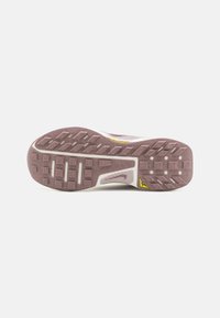 Sål af en Nike trail løbesko med brun tekstureret greb, hvid mellemsål og gul logo på en hvid baggrund.