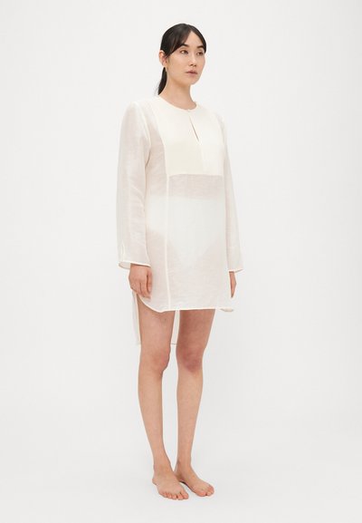 Vestito crema leggero e trasparente con maniche lunghe, scollo con bottoni e spacchi laterali, caratterizzato da una sezione corporea testurizzata.