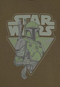 T-shirt marrone con una grafica di un personaggio con elmetto che tiene un blaster, con testo "Star Wars" e accenti di sfondo verdi.