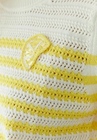 White and yellow striped crocheted fabric with a small yellow crocheted lemon slice embellishment.