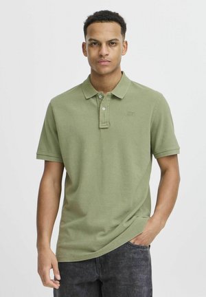 Oliven grønn polo skjorte med teksturert stoff, korte ermer, tre-knapps placket og logo brodert på brystet. Kombinert med mørke jeans.