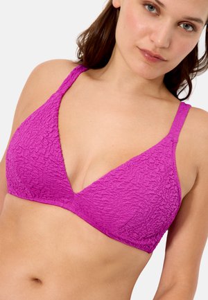 Mujer con un bralette texturizado color magenta con tirantes delgados, mostrada desde el torso medio hasta por encima de la cabeza sobre un fondo liso.