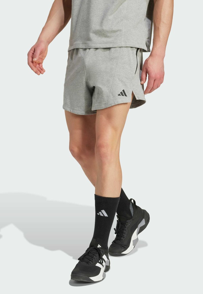 Shorts de sport gris avec fentes sur les côtés, associés à des chaussettes noires et des chaussures avec un logo blanc. Le tissu semble doux et léger.