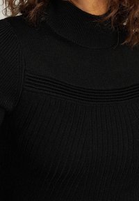 Pull noir côtelé avec un col montant et des panneaux texturés horizontaux sur la poitrine. Il est fabriqué en maille douce et présente une coupe ajustée.