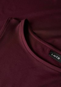 Burgundy t-shirt with a crew neckline, made from smooth fabric, featuring a subtle sheen and stitched detailing near the collar. Brand tag visible.