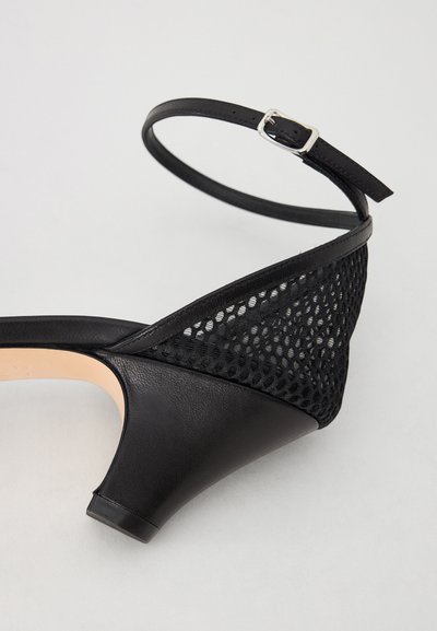 Black heeled shoe featuring a mesh fabric upper, leather accents, and a slender ankle strap with a silver buckle. Rounded heel design.