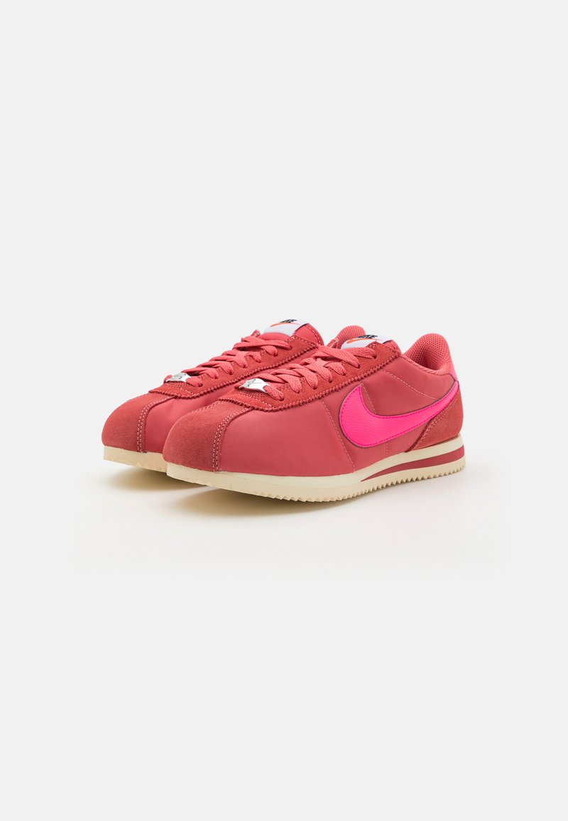 Baskets rouges avec un matériau lisse et un swoosh en cuir rose. Embout arrondi, design à lacets et semelle texturée. Style rétro classique.