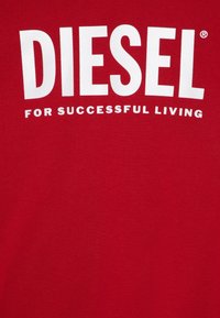 Röd tyg med stor vit text "DIESEL" och mindre text nedanför "FÖR FRAMGÅNGSRIKT LIV" tryckt på det.