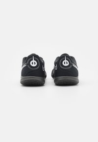 Para czarnych halowych butów piłkarskich Nike, widok z tyłu, z białym logo Swoosh i okrągłą grafiką na pięcie.
