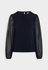 Haut marine avec des manches longues en mesh transparent à pois et un col rond. Présente une fermeture arrière en forme de clé et un corps lisse et uni.