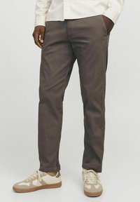 Braune Baumwollchinos mit geradem Schnitt, ausgestattet mit Seitentaschen. Kombiniert mit beigen und hellbraunen Sneakers.