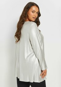 Silver långärmad topp med en glittrig textur, lös passform och sidofickor, kombinerad med svarta leggings.