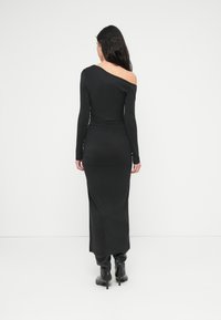 Μαύρο φόρεμα με μακριά μανίκια, με έναν ακάλυπτο ώμο, εφαρμοστή σιλουέτα, λεία υφή και μακρύ τελείωμα, φορεμένο με μαύρες μπότες μέχρι το γόνατο.