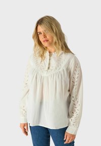 Blusa di cotone bianca con maniche lunghe, dettagli ricamati lungo le spalle e le maniche, abbottonatura e taglio morbido.