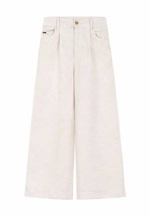 Beżowa bluza z nadrukiem graficznym włożona w białe sztruksowe spodnie z wysokim stanem, z widocznymi tylnymi kieszeniami i małą materiałową metką.