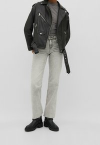 Veste de moto en cuir noir avec des éléments en métal argenté, t-shirt gris ajusté, jeans droits gris clair et bottines à talons en noir.