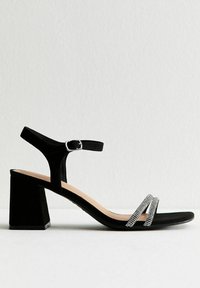 Sandalo con tacco blocco nero caratterizzato da cinturini in suede, una fascia alla caviglia con fibbia e due bande diagonali decorate con strass che attraversano il piede.