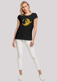 Black short-sleeve t-shirt featuring a yellow and white cartoon character graphic. Paired with white slim-fit pants and white sneakers.