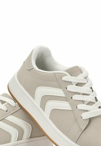 Zapatillas de deporte gris claro con una textura suave, cordones blancos y franjas de acento blancas. Cuentan con una suela de goma y un collarín acolchado.