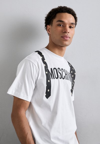 Baltas T-krekls ar melnu tekstu "MOSCHINO" un polka punktu piekariņiem grafiku. Īsas piedurknes, apaļa kakla izgriezums, kokvilnas materiāls.