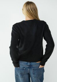 Zwarte gebreide trui met lange mouwen, ronde hals en zachte textuur. Gecombineerd met middelblauwe denim jeans met achterzakken.