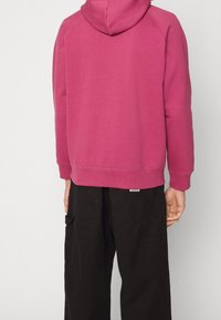 Fleece hoodie in effen magenta met een kangoeroezak en kap. Gepaard met zwarte cargo broeken met meerdere zakken en een gestructureerde stof.