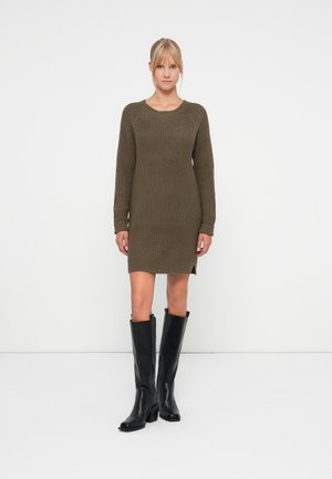 Robe pull en tricot vert olive, texture côtelée, manches longues, col rond, fentes latérales, associée à des bottes en cuir noires hautes.