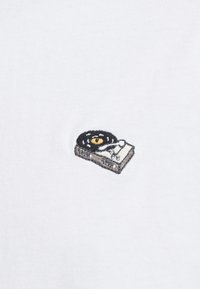 Petit disque vinyle noir brodé et platine blanche sur fond en tissu blanc.
