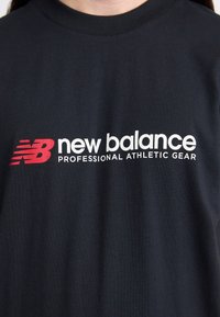 Sort bomulds t-shirt med et stort hvidt "new balance" logo og et rødt "NB" symbol på forsiden. Enkel design med rund hals.