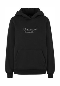 Felpa nera con cappuccio, dotata di tasca frontale, polsini a coste e una frase in arabo insieme al testo inglese che recita "Ama te stesso prima di tutto."