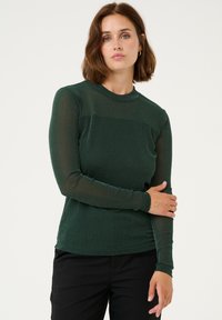 Lange mouwen groene top met een gestructureerde, glanzende afwerking, voorzien van een ronde hals en een aansluitend design, gecombineerd met zwarte broek.