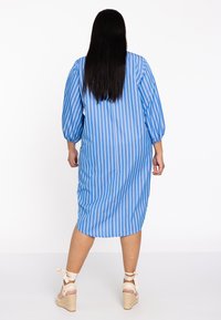Blauw gestreepte jurk met lange, puffed mouwen, knielange snit, zachte stof en een relaxte pasvorm. Gepaard met sleehakken met enkellussen.