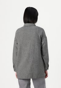 Hedvábný košile vzoru houndstooth v černobílé barvě s límečkem, dlouhými rukávy a volným střihem, zobrazená zezadu na bílém pozadí.