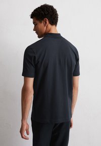 Short-sleeve polo shirt in dark navy, textured fabric, with a collar and a straight hem. Features side slits and simple stitching details.