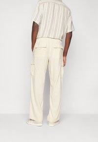 Löst sittande, krämfärgade byxor har cargofickor och ett elastiskt midjeband. Tyget har en texturerad yta som förbättrar andningsförmågan.